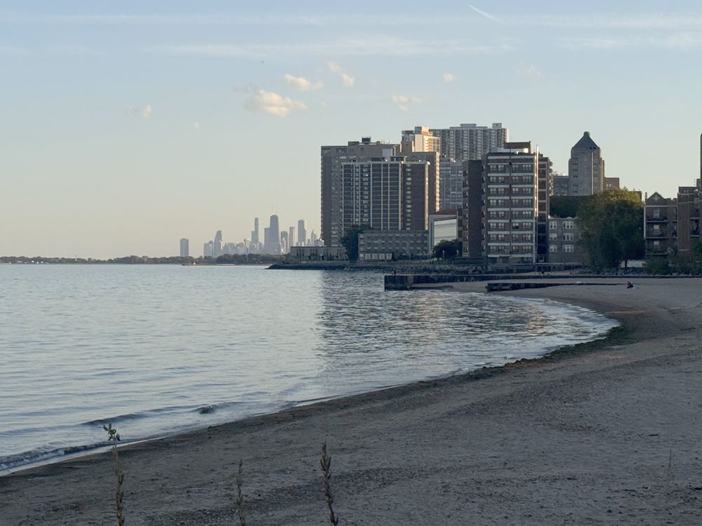 A quiet Rogers Park beach at golden hour, with lakefront buildings and the Chicago skyline in the distance